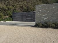 a brick wall with two sections of a concrete driveway and bushes in front of it