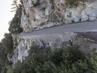 a motorcycle drives on the road near the rocks by the mountain side, making its way up the cliff face