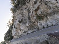 a motorcycle drives on the road near the rocks by the mountain side, making its way up the cliff face