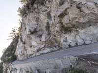 a motorcycle drives on the road near the rocks by the mountain side, making its way up the cliff face