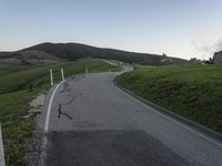 there is a white motorcycle riding on the road towards a green hill and a house