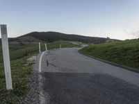 there is a white motorcycle riding on the road towards a green hill and a house