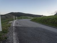 there is a white motorcycle riding on the road towards a green hill and a house