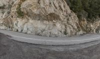 a motorcyclist on the road in front of an alpine mountain cliff side