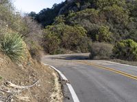 a motorcycle driving down a winding road with trees and hills in the background next to it