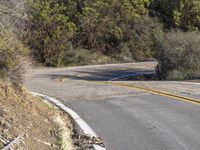 a motorcycle driving down a winding road with trees and hills in the background next to it