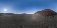 a mountain covered in black sand and a small rock pile on top of it on a sunny day