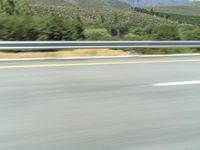 a motorcycle riding down the highway in the mountains of california with blurry air and trees below