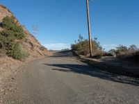 a narrow dirt road is surrounded by shrubs and power lines above the hill top with telephone wires on each side