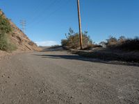 a narrow dirt road is surrounded by shrubs and power lines above the hill top with telephone wires on each side