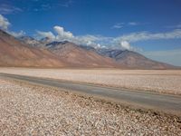 a car is parked on a gravel road by mountains near an empty road and dry, rocky terrain