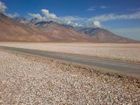 a car is parked on a gravel road by mountains near an empty road and dry, rocky terrain