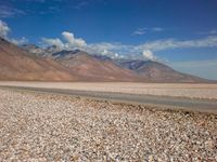 a car is parked on a gravel road by mountains near an empty road and dry, rocky terrain