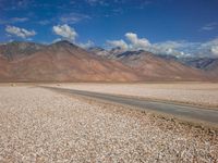 a car is parked on a gravel road by mountains near an empty road and dry, rocky terrain