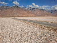 a car is parked on a gravel road by mountains near an empty road and dry, rocky terrain