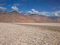 a car is parked on a gravel road by mountains near an empty road and dry, rocky terrain