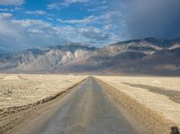 a lone road surrounded by mountains under a cloudy sky at sunset or sunrise light, near some rocky hills