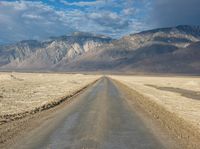 a lone road surrounded by mountains under a cloudy sky at sunset or sunrise light, near some rocky hills