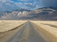 a lone road surrounded by mountains under a cloudy sky at sunset or sunrise light, near some rocky hills