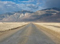 a lone road surrounded by mountains under a cloudy sky at sunset or sunrise light, near some rocky hills