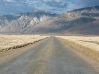 a lone road surrounded by mountains under a cloudy sky at sunset or sunrise light, near some rocky hills