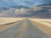 a lone road surrounded by mountains under a cloudy sky at sunset or sunrise light, near some rocky hills