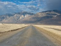 a lone road surrounded by mountains under a cloudy sky at sunset or sunrise light, near some rocky hills