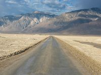 a lone road surrounded by mountains under a cloudy sky at sunset or sunrise light, near some rocky hills