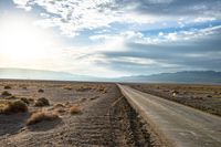 there is a empty road between the mountains and a grassy field with desert land on either side