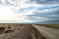 there is a empty road between the mountains and a grassy field with desert land on either side