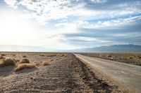 there is a empty road between the mountains and a grassy field with desert land on either side