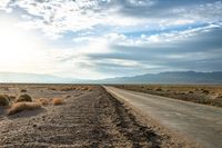 there is a empty road between the mountains and a grassy field with desert land on either side