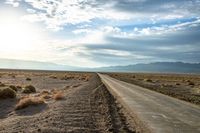 there is a empty road between the mountains and a grassy field with desert land on either side