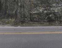 a motorcycle sits on the side of the road near a rock formation on a mountain