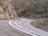 a motorcycle rider rides down a winding mountain road past the rocks and mountainside a hill with some trees