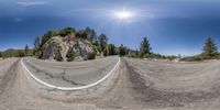 a 360 - angle photograph of the road winding off a mountain side and sun shining above