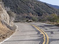 two roads passing a steep cliff side side and one lane is closed with one red stop sign