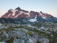 rocks and grass growing in the mountains at sunset with snow on top of them and two snow - capped peaks in distance