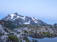 rocks and grass growing in the mountains at sunset with snow on top of them and two snow - capped peaks in distance