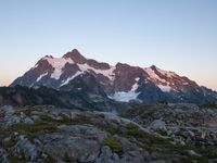 rocks and grass growing in the mountains at sunset with snow on top of them and two snow - capped peaks in distance