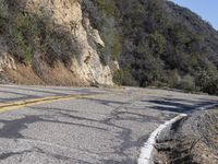 a group of bikers riding down the road by a cliff and a mountain side