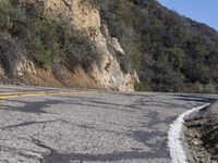 a group of bikers riding down the road by a cliff and a mountain side