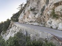 a person is on a motorcycle on a cliff road at the foot of a mountain