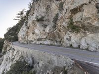 a person is on a motorcycle on a cliff road at the foot of a mountain