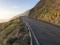 road going up the side of the mountain beside a cliff overlooking ocean at sunset with people riding bikes