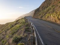 road going up the side of the mountain beside a cliff overlooking ocean at sunset with people riding bikes