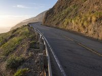 road going up the side of the mountain beside a cliff overlooking ocean at sunset with people riding bikes