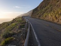 road going up the side of the mountain beside a cliff overlooking ocean at sunset with people riding bikes