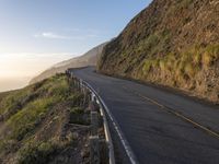 road going up the side of the mountain beside a cliff overlooking ocean at sunset with people riding bikes