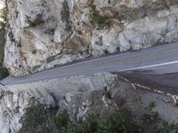 the side of a cliff with cars traveling down it and people walking on a street below